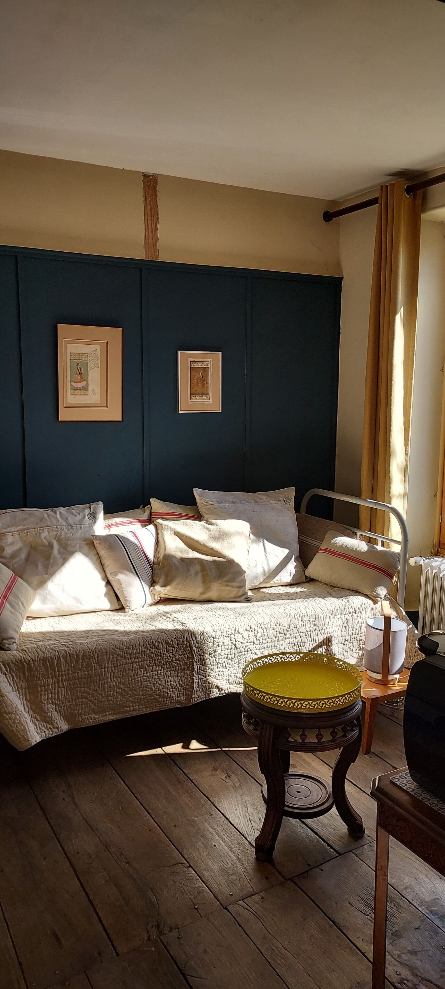 A room with a bed, a small table with a cup, and framed pictures on the wall.