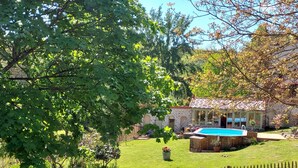A backyard with a swimming pool, a wooden deck, and a stone house. - Maison Volière (La Souterraine)