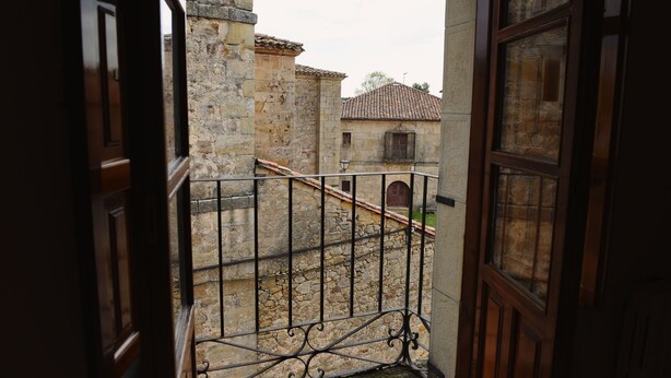 Un bâtiment en pierre avec un toit recouvert de tuiles, une rambarde en métal et une porte en bois.
