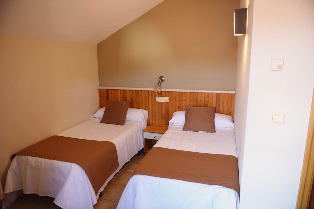 Ein Hotelzimmer mit zwei Einzelbetten, Holzvertäfelung an den Wänden, einem kleinen Nachttisch und einer Wandleuchte.