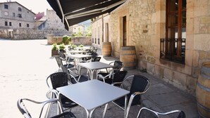 Un café en plein air avec des tables et des chaises, des murs en pierre et des tonneaux en bois.