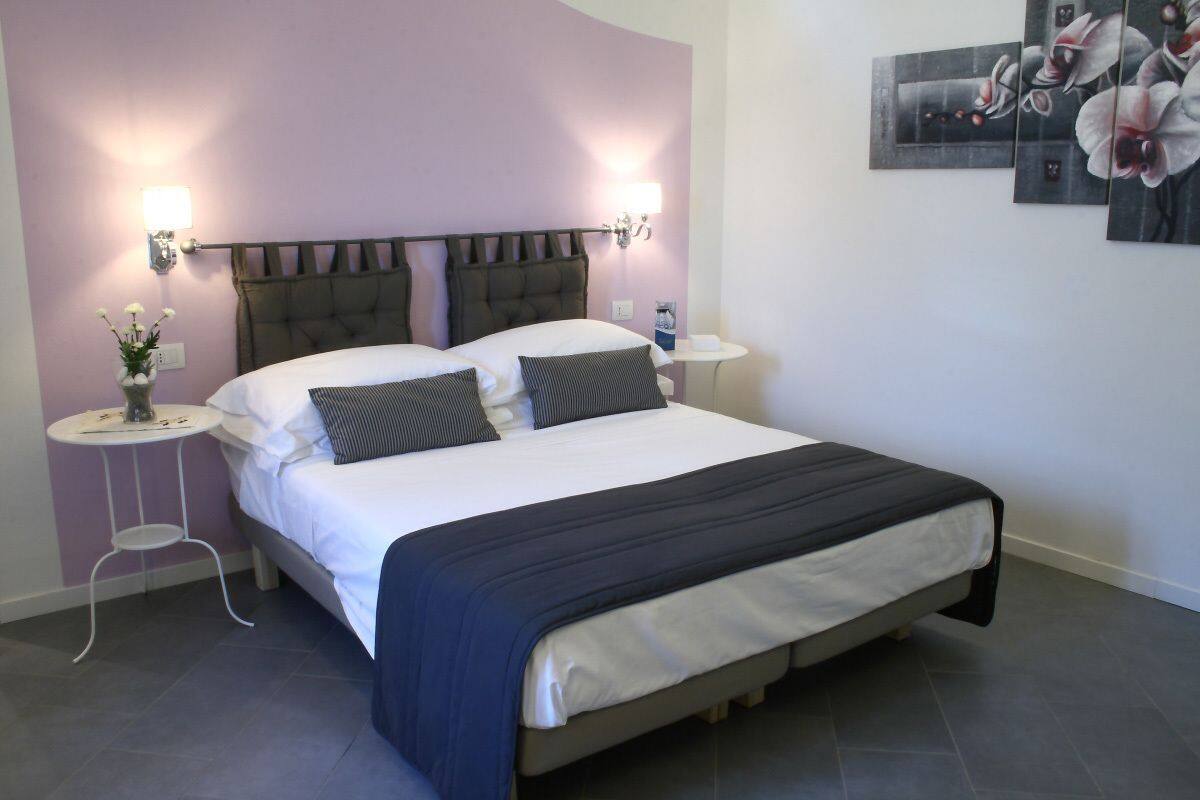 A bedroom with a bed, two bedside tables, a wall-mounted lamp, and a small table with a vase of flowers.