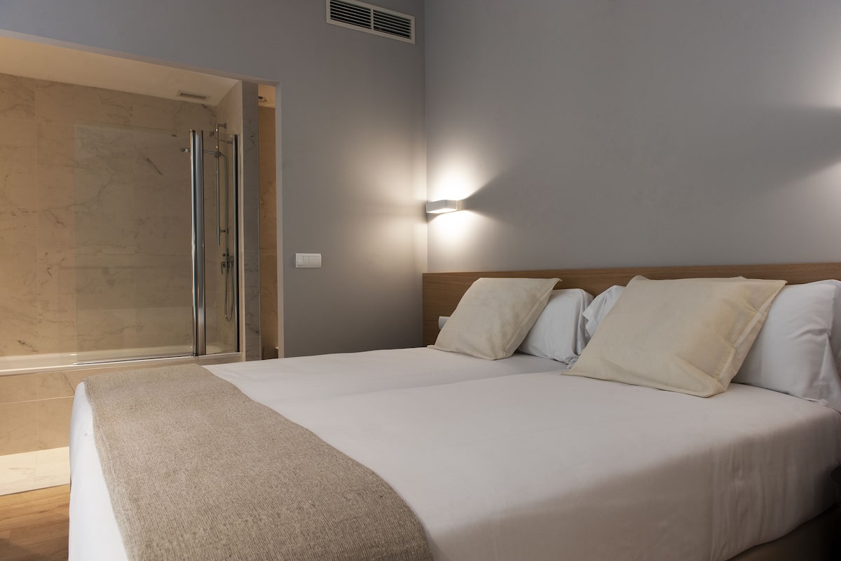 A hotel room with a bed, a shower, and a wall-mounted light.