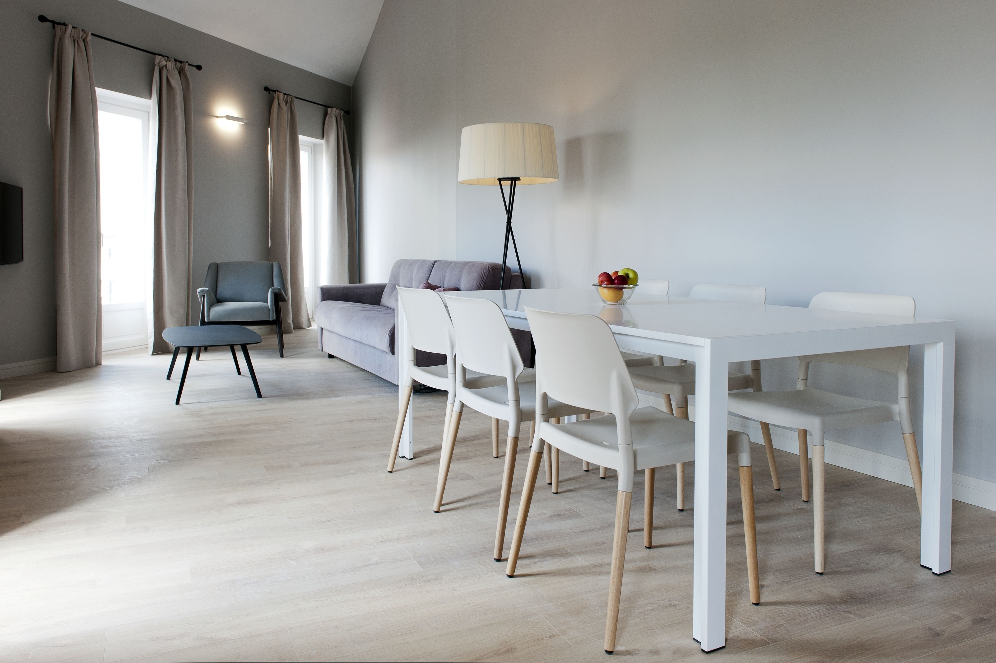 En moderne stue med et hvidt spisebord, hvide stole, en grå sofa og en blå lænestol.