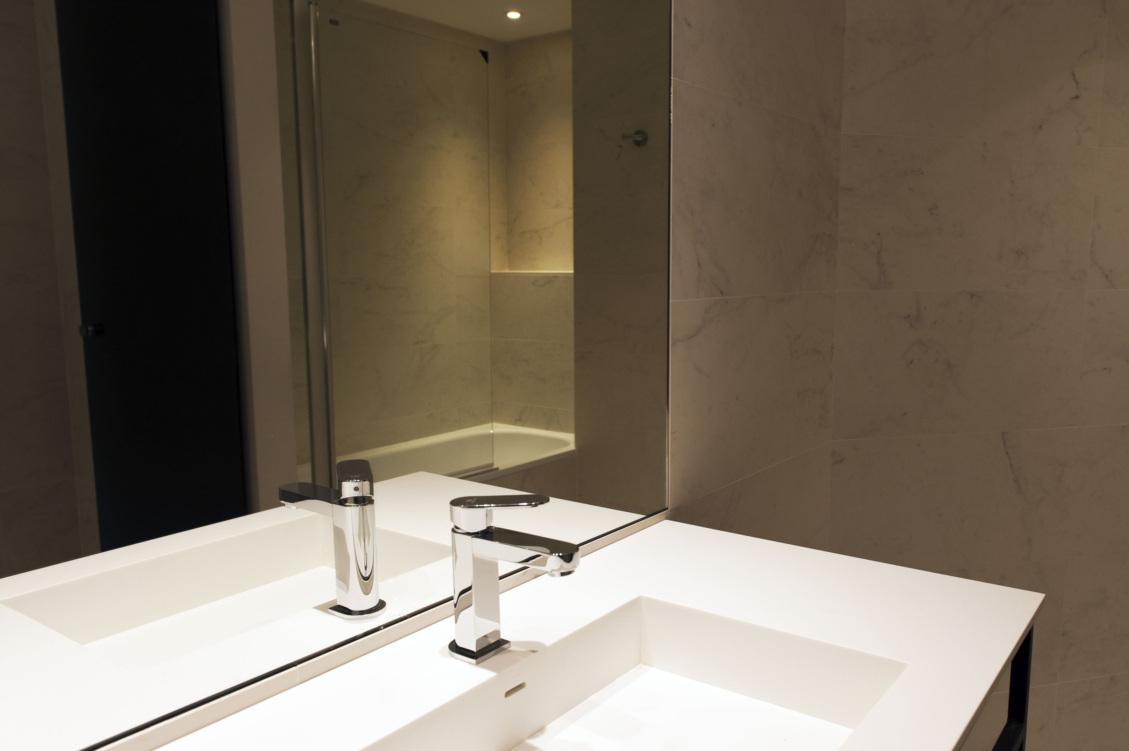 A modern bathroom with a large mirror, two sinks, and a shower.