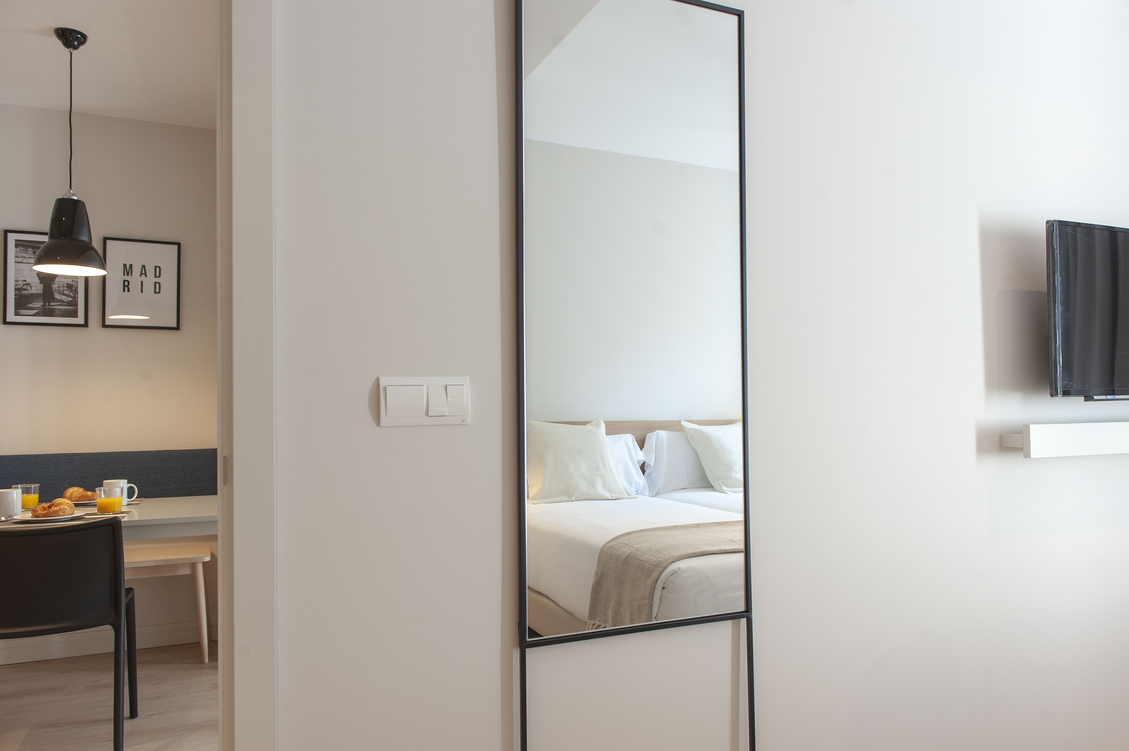 Une chambre d’hôtel moderne, équipée d’un lit, d’une table de chevet et d’un grand miroir qui reflète la pièce.