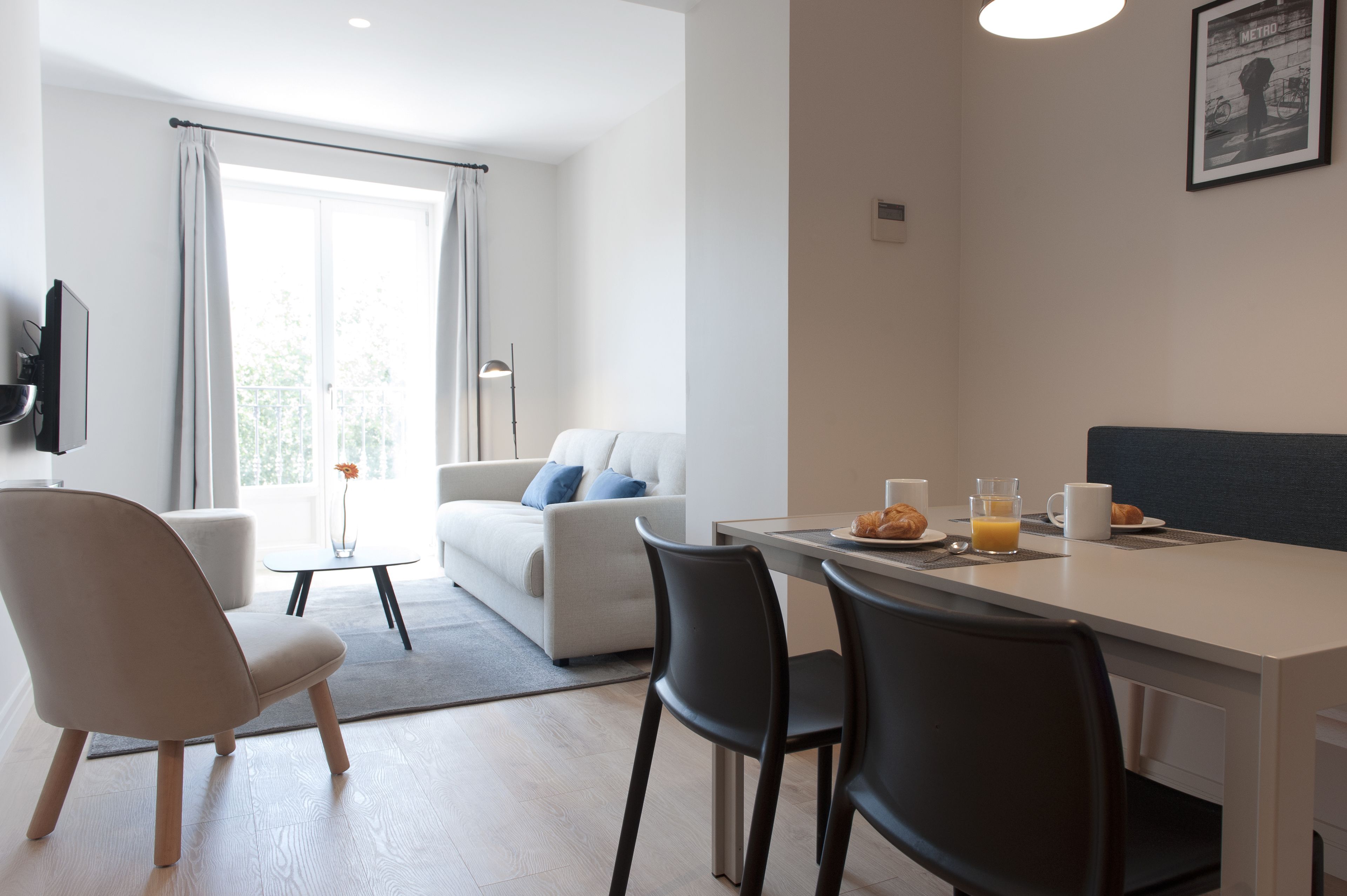 Habitación de hotel moderna con comedor, sofá, sillón y mesa preparada para el desayuno.