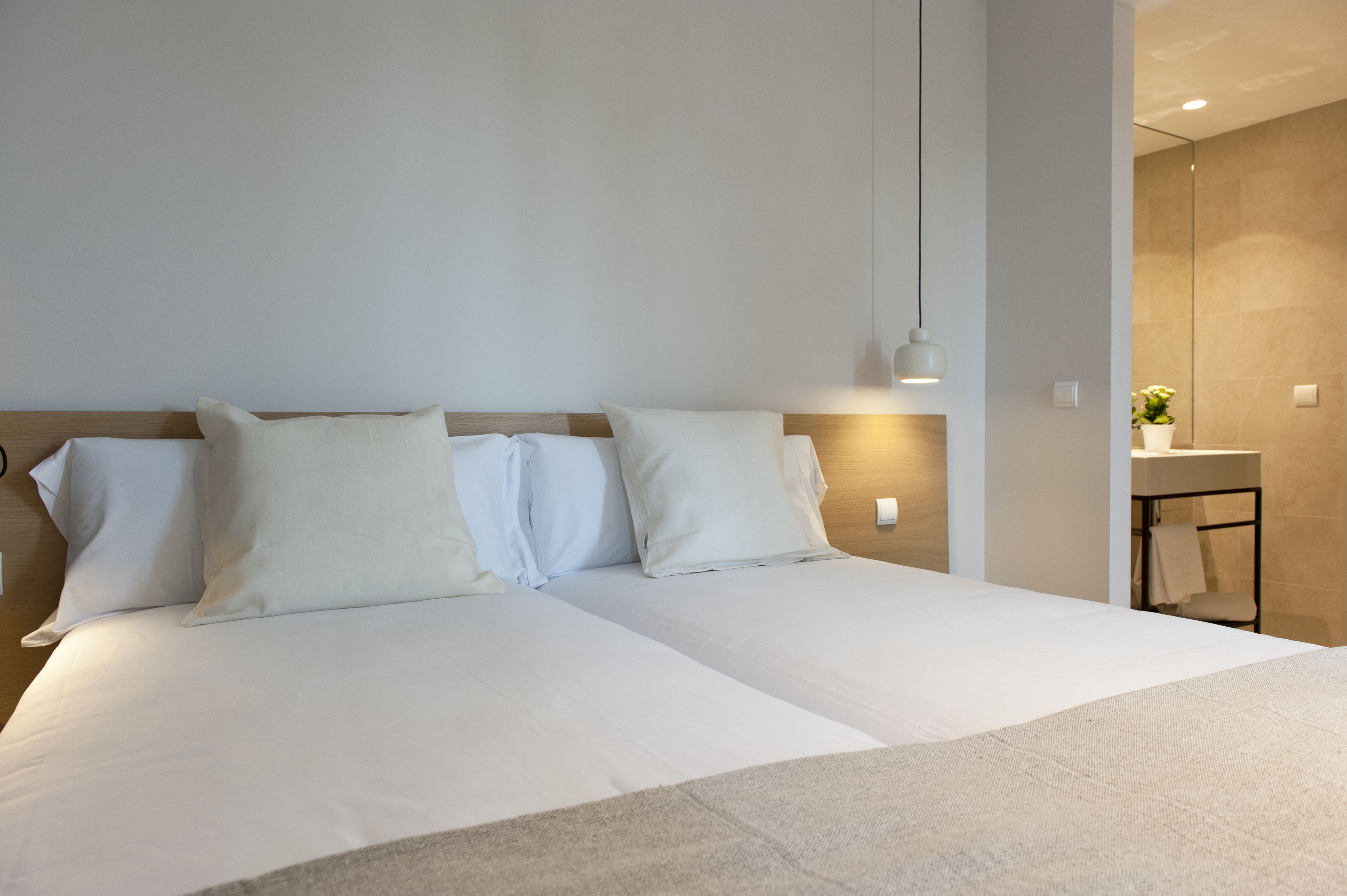 A modern hotel room with a large bed, a bedside table, and a small bathroom visible through an open door.