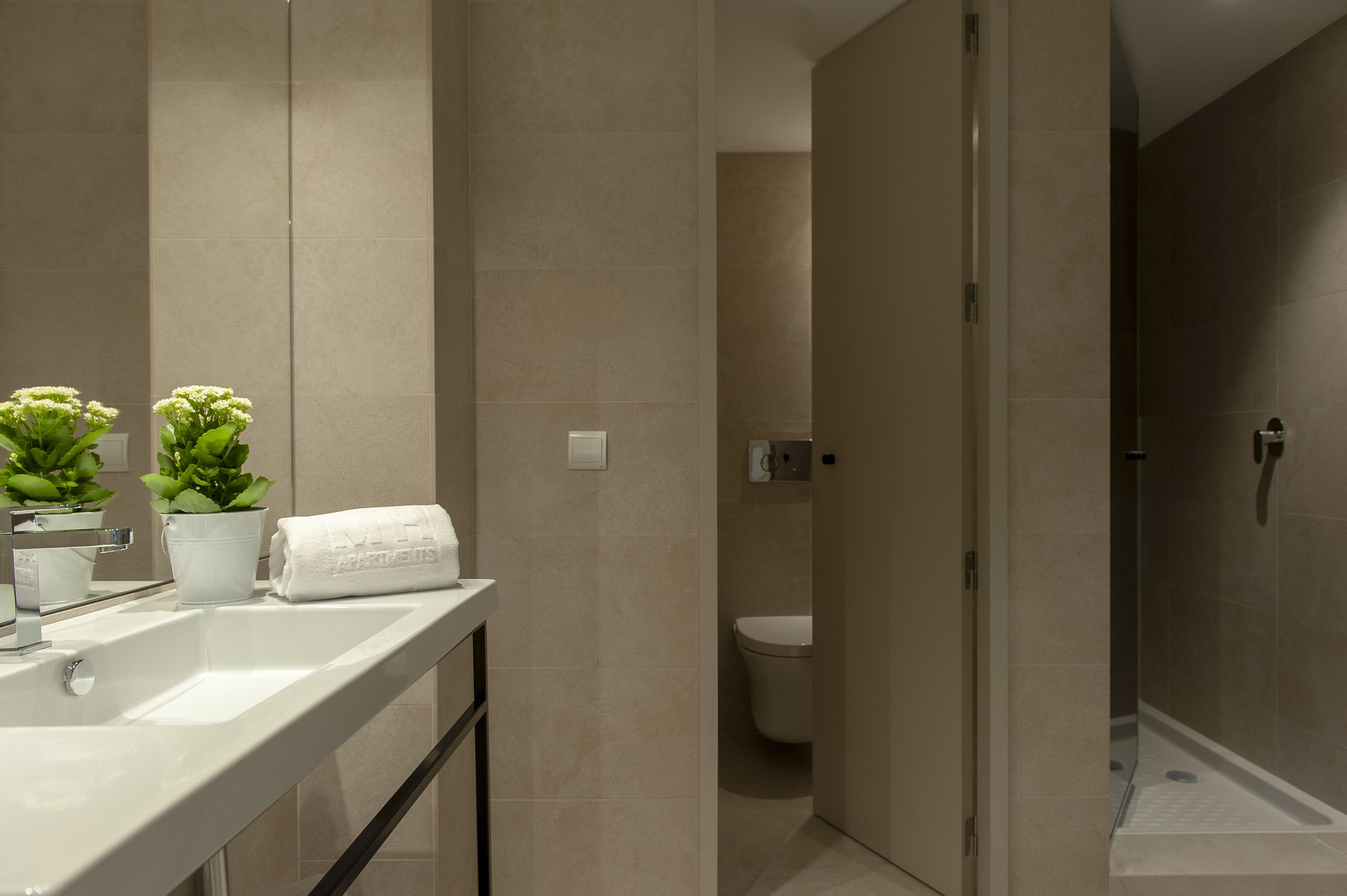 A modern bathroom with a white sink, two potted plants, a white towel, and a toilet.