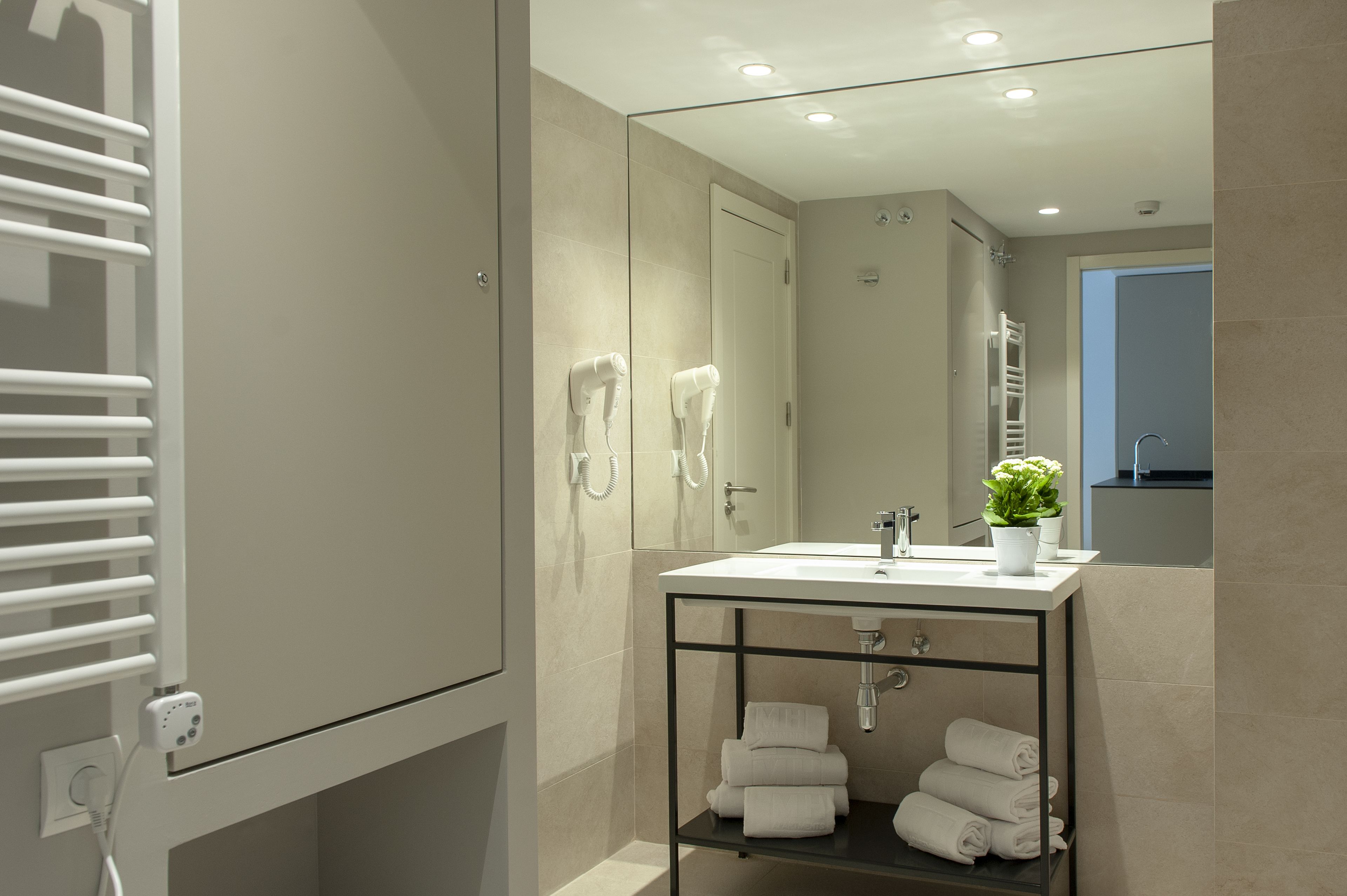 A modern bathroom with a large mirror, a sink with a potted plant, and a towel rack with towels.