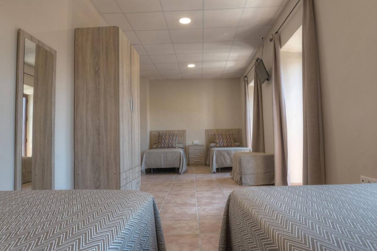 A hotel room with two beds, a wooden wardrobe, a small table, and a window with curtains.