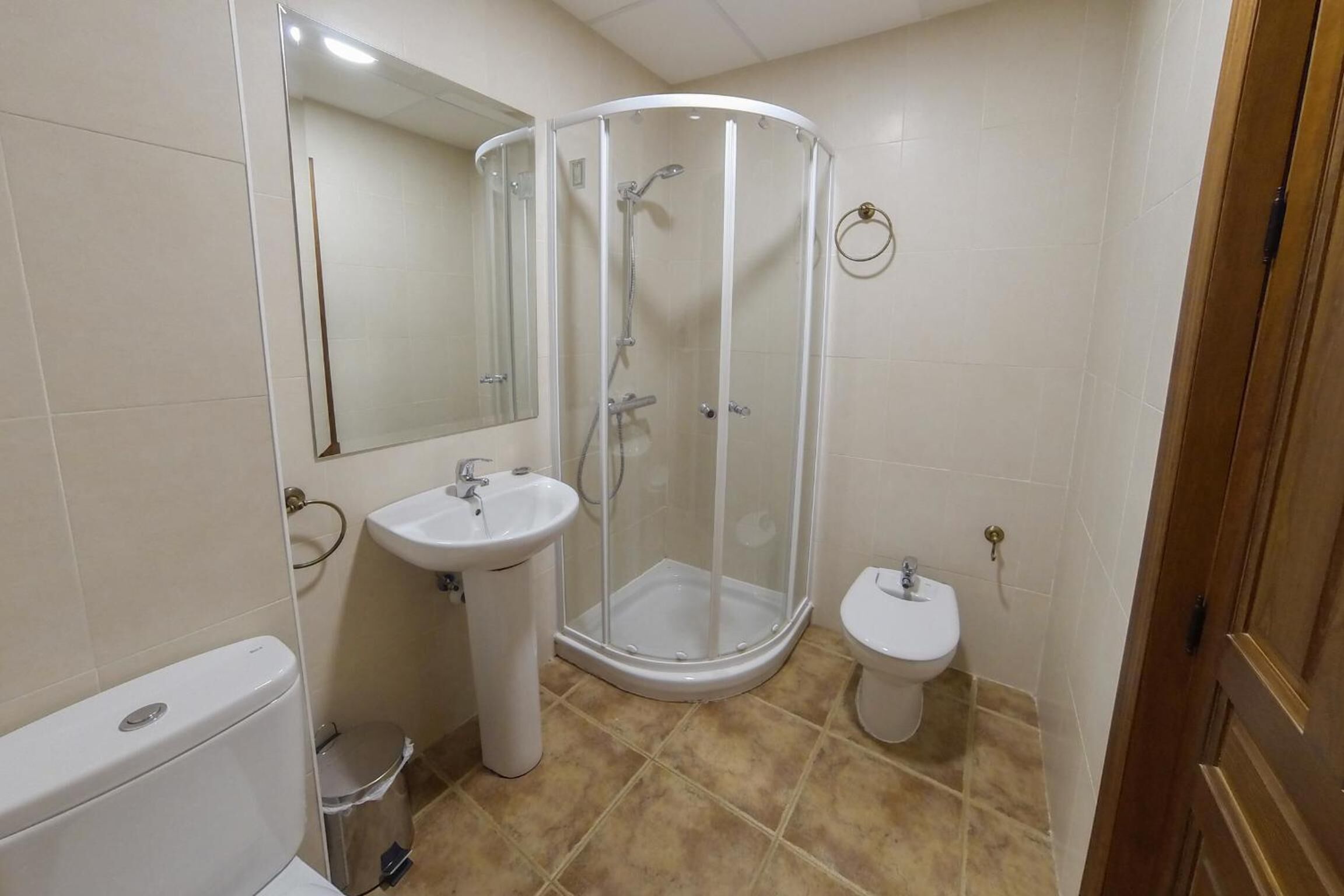 Een badkamer met douche, wastafel, toilet en spiegel.
