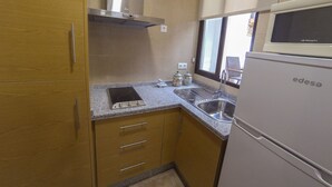 Una cocina compacta con armarios de madera, estufa integrada, microondas y un lavamanos.