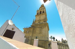 Un edificio histórico con una imponente torre de campanas, rodeado de construcciones modernas.