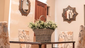 Una cesta de mimbre con flores sobre una mesa de cristal, rodeada de sillas estampadas, con espejos decorativos en las paredes.