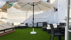 Un patio en la azotea con césped artificial, mobiliario de exterior y un gran paraguas.