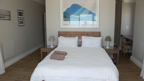 A neatly made bed with white linens and two brown towels, a wooden headboard, two bedside tables with lamps, and a framed picture of Snowdonia on the wall. - Cape Town Kite Club (Cape Town)