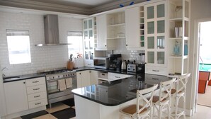 A modern kitchen with white cabinets, a black countertop, and a central island with bar stools. - Cape Town Kite Club (Cape Town)