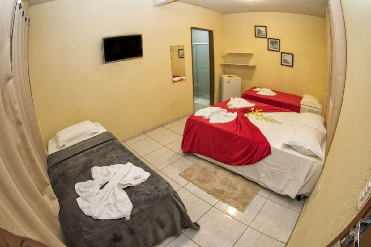 Ein Hotelzimmer mit zwei Betten, einem Fernseher, einem Spiegel und einem kleinen Badezimmer.