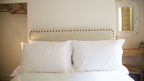 Ein Bett mit weißen Leinen, ein Kopfstück mit dekorativem Muster und ein Nachttisch aus Holz mit Spiegel und kleiner Ablagefläche.