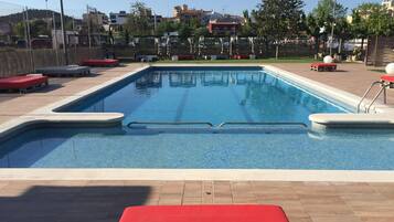 Une piscine rectangulaire à l’eau d’un bleu limpide, entourée d’une terrasse carrelée avec des chaises longues rouges et d’un espace de terrasse en bois.