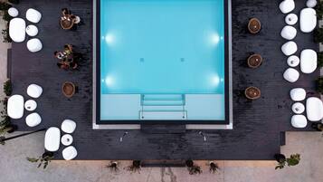 A rooftop pool area with a rectangular pool, surrounded by white lounge chairs and potted plants.