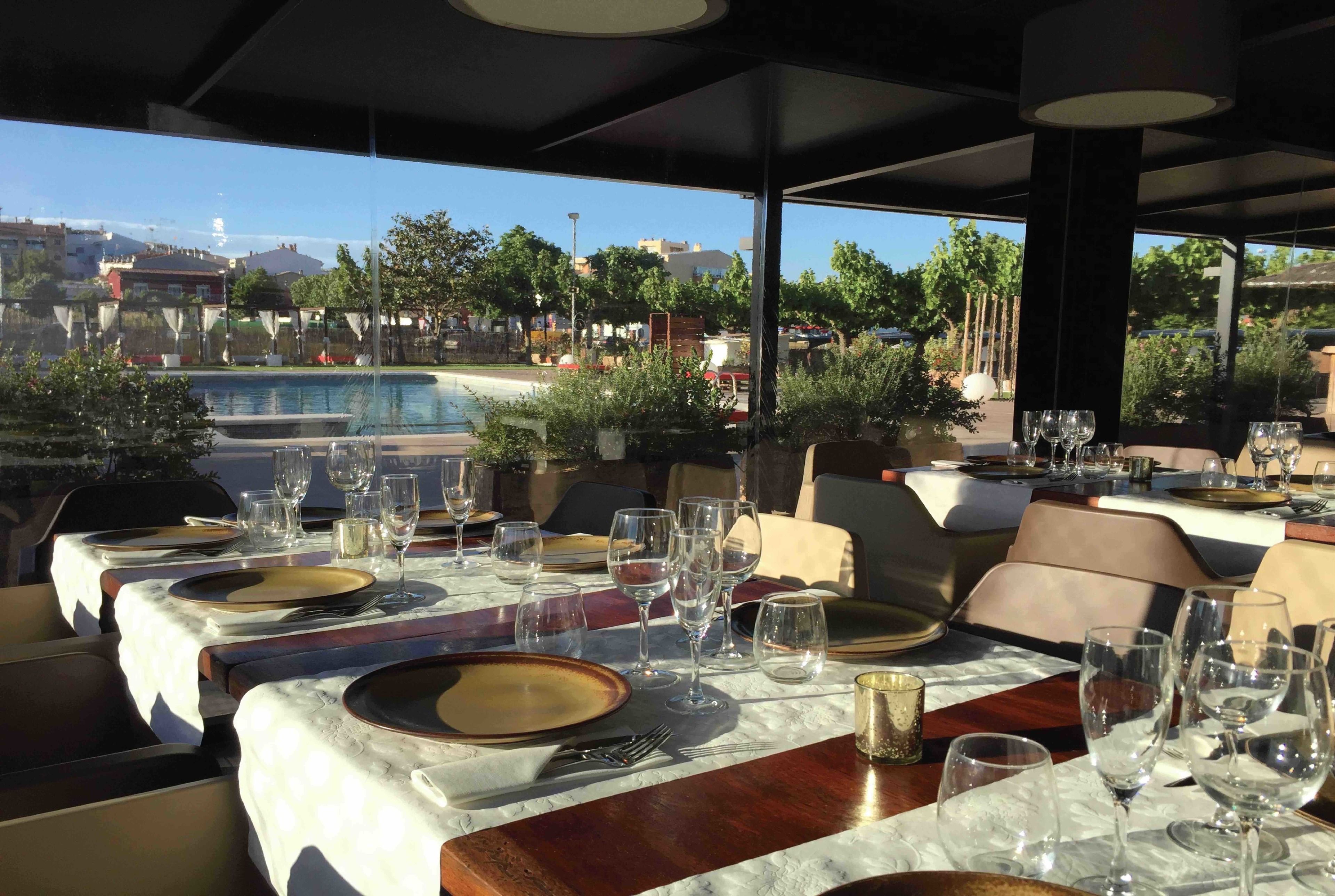 Un restaurante con mesas preparadas para comer, con vista a una piscina y edificios al fondo.