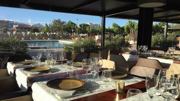 Un restaurante con mesas preparadas para comer, con vista a una piscina y edificios al fondo.