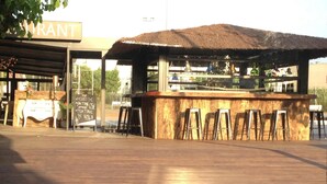 An outdoor bar area with a thatched roof, bar stools, and a chalkboard menu. - Hostal Solfina (Palafolls)