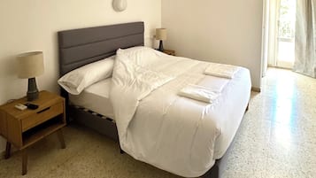Een net opgemaakt bed met witte lakens, twee nachtkastjes met lampen, en een lichtschakelaar op het linker nachtkastje.