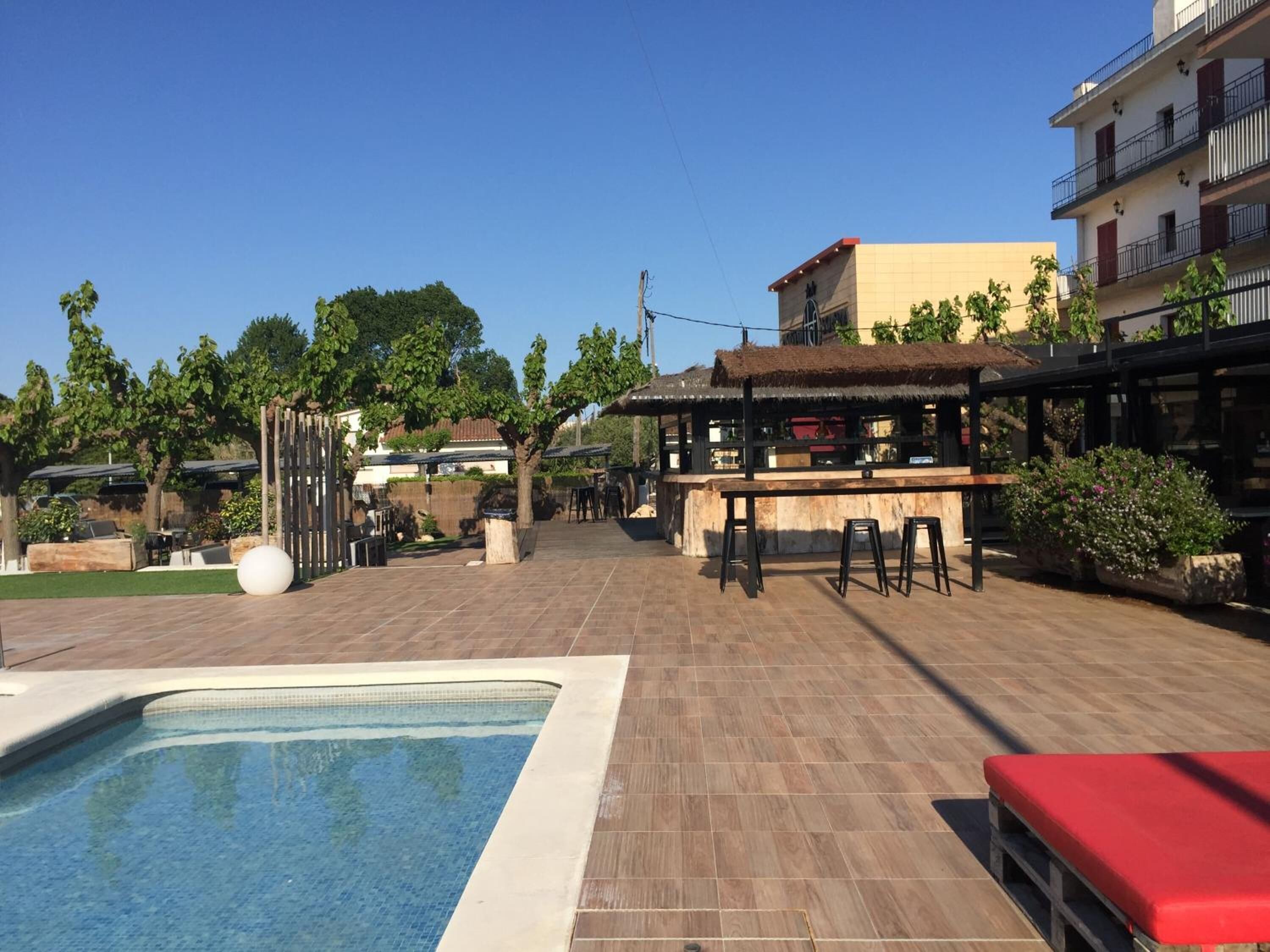 A pool area with a bar and seating, surrounded by buildings and greenery.