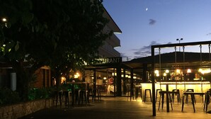 An outdoor restaurant area with a wooden deck, tables, and chairs. - Hostal Solfina (Palafolls)
