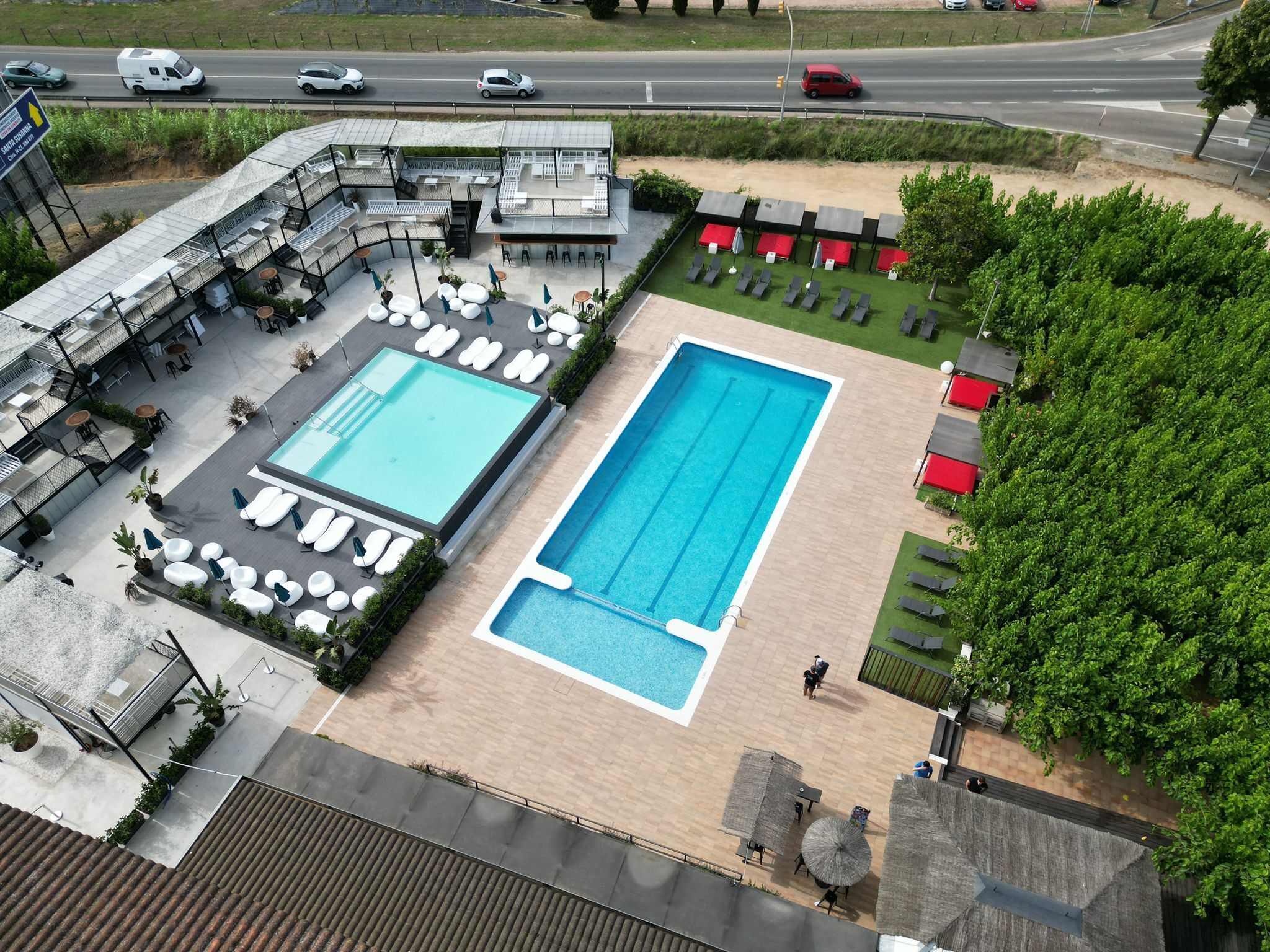 Área de piscina no terraço com duas piscinas, cadeiras de sol e um espaço de estar com guarda-sóis.