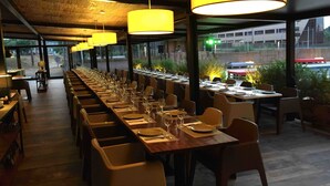 A long dining table with chairs, yellow pendant lights, and a view of the city through large windows. - Hostal Solfina (Palafolls)