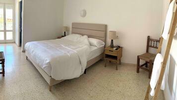 Um quarto com cama, mesas de cabeceira, uma cadeira e uma janela.