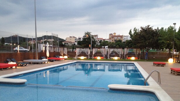 A rectangular swimming pool with a tiled edge, surrounded by lounge chairs and a covered seating area. - Hostal Solfina (Palafolls)