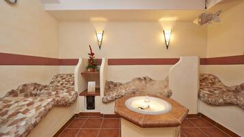 Una stanza spa con panche a mosaico, un lavabo centrale e luci a parete.