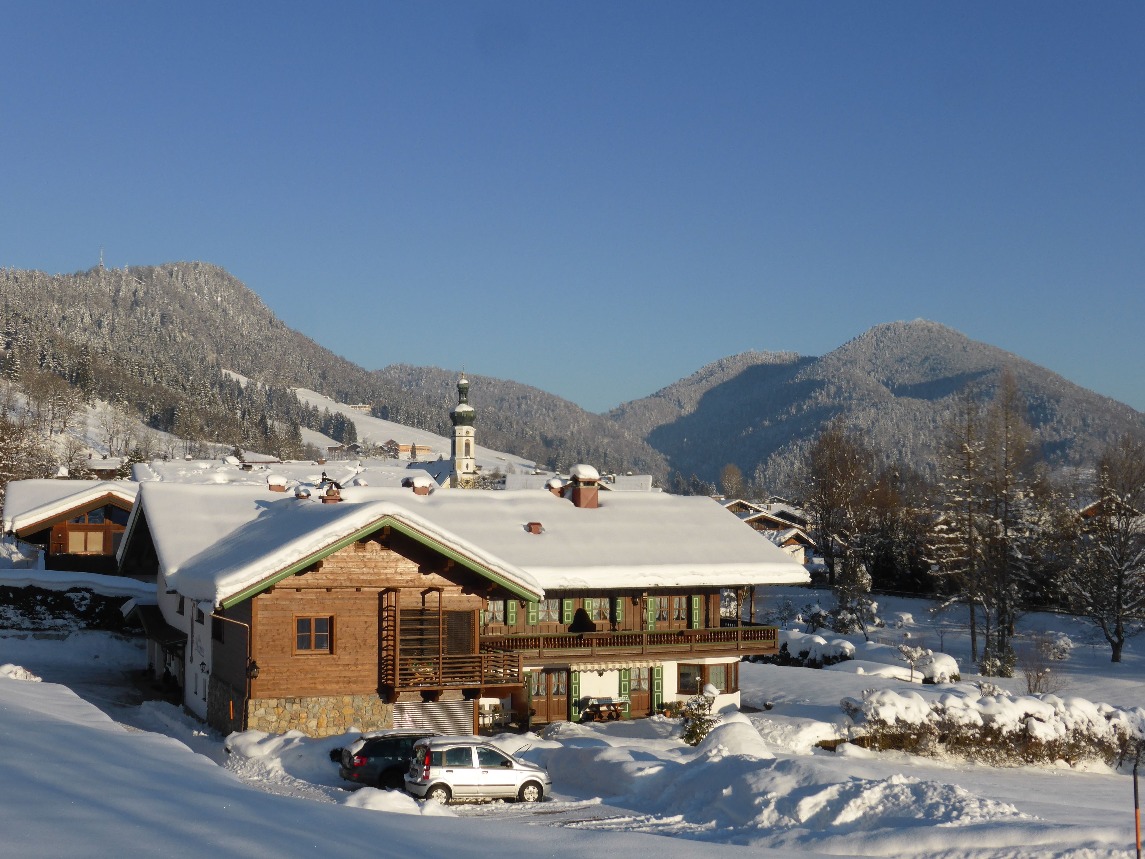 Un chalet en bois, avec un toit enneigé, un balcon et une vue sur les montagnes.