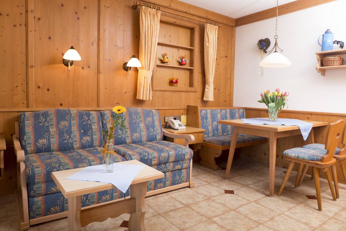 A cozy room with a sofa, a small table, a dining table, and chairs. There is a telephone on the sofa and a vase with flowers on the dining table.
