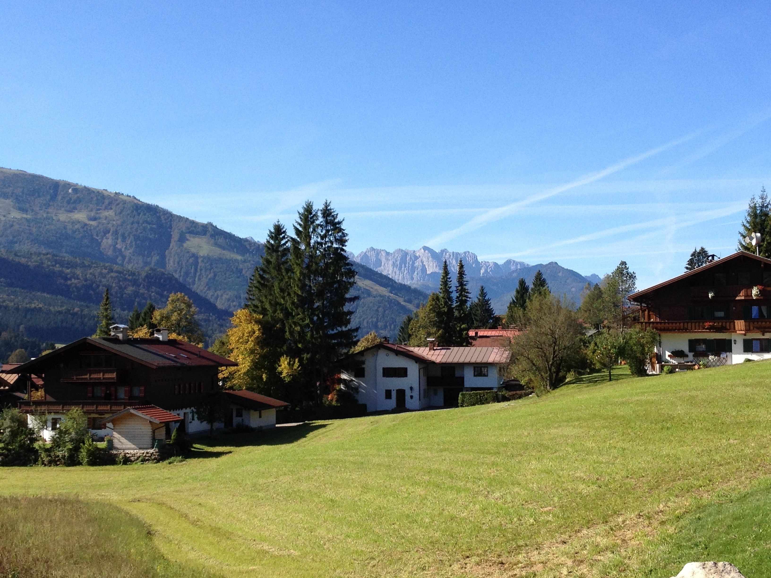Un village de montagne isolé, avec ses maisons traditionnelles en bois, une colline verdoyante et, en toile de fond, un paysage montagneux.