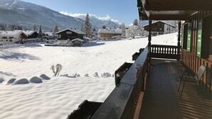 Ein schneebedecktes Dorf mit Holzhäusern, einem Balkon mit Geländer und einem Berg im Hintergrund.