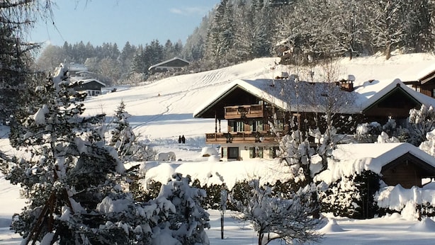 Ein mit Schnee bedecktes Chalet mit mehreren Hütten, umgeben von Bäumen und einer verschneiten Landschaft.