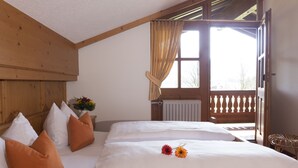 Ein Doppelbett mit weißen Leinen, zwei orangefarbene Kissen und eine Vase mit Blumen.