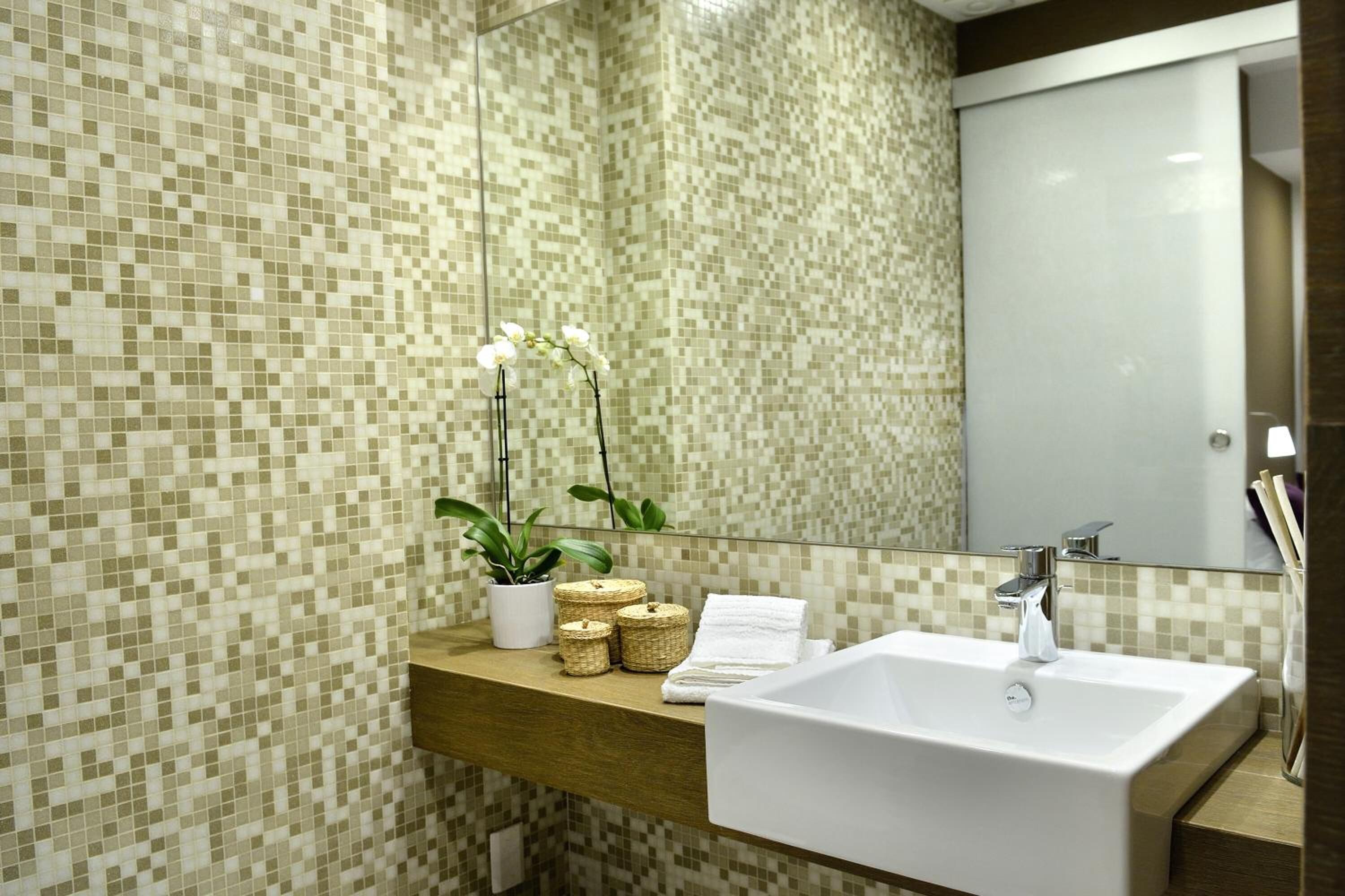 A bathroom with a tiled mosaic wall, a wooden countertop, a white sink, and a mirror.