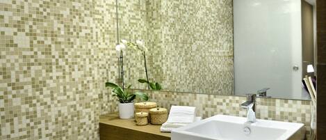 A bathroom with a tiled mosaic wall, a wooden countertop, a white sink, and a mirror.