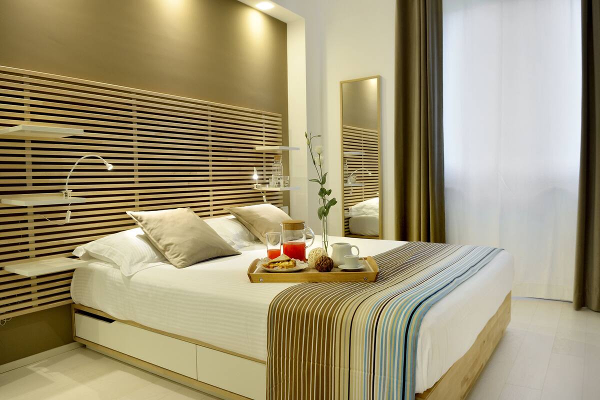 Ein modernes Hotelzimmer mit einem großen Bett, einem Holzkopfende, Nachttischen und einem Tablett mit Frühstücksgebäck.