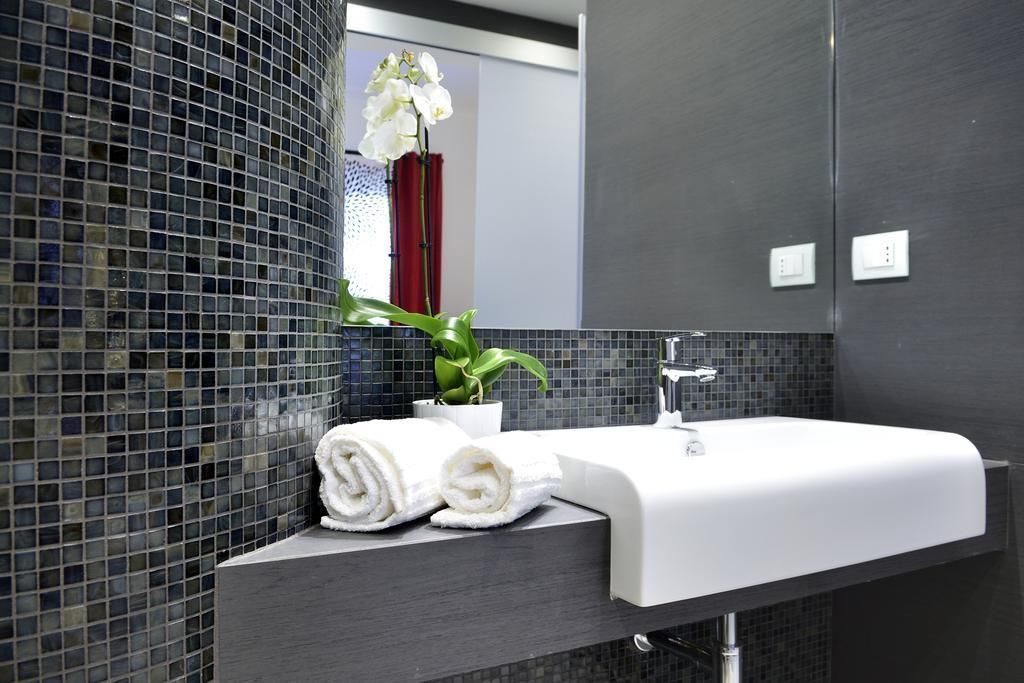 Un baño moderno con un lavabo blanco, paredes con azulejos oscuros y una orquídea en maceta.