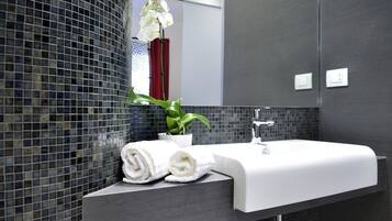 Un baño moderno con un lavabo blanco, paredes con azulejos oscuros y una orquídea en maceta.