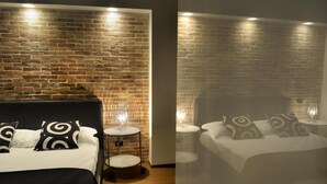 A hotel room with a brick wall, a bed with black and white patterned pillows, and a bedside table with a lamp. - Baglio Caruana Cantina & Relais (Siculiana)