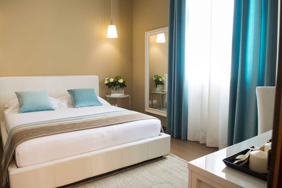 Ein Schlafzimmer mit einem großen Bett, Nachttischen, einem Spiegel und einem Fenster mit Vorhängen.
